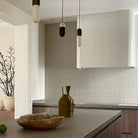 The Sevilla Mosaic Tiles, Original KitKat design in a Cafe Latte, with a size of 20x145mm installed on a wall in a kitchen. A white range hood installed on top and cabinetry below. Island bench cabinetry with a vase and apple bowl resting on top. A plant pot to the left in a separate room.