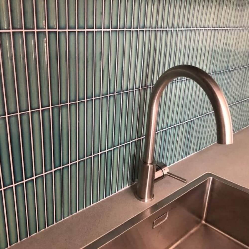 The Sevilla Mosaic Tiles, Original KitKat design in a forest green glossy, with a size of 20x145mm installed on a wall with a counter top, sink basin and faucet mounted in front