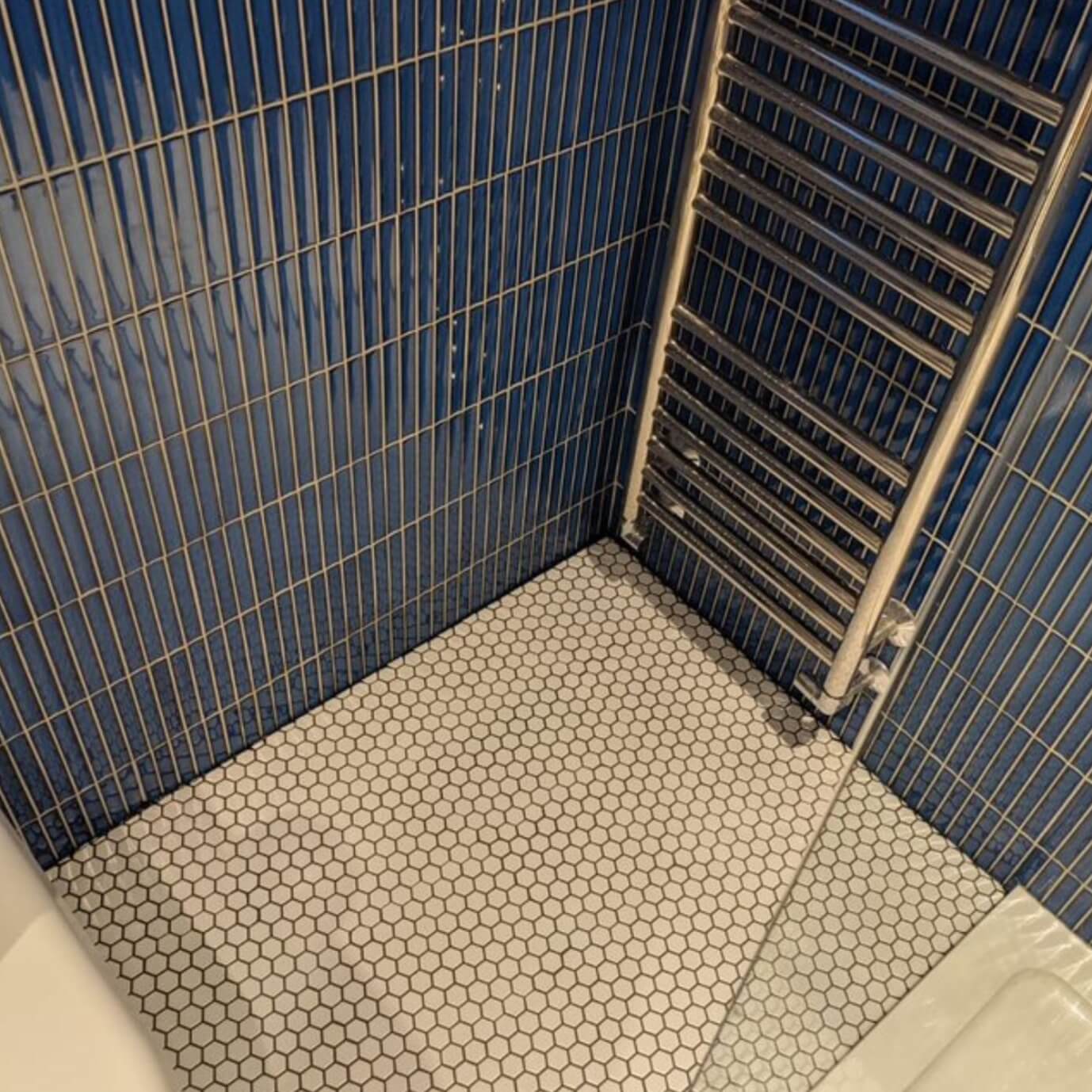 The Sevilla Mosaic Tiles, Original KitKat design in a Jeans Blue, with a size of 20x145mm installed in a bathroom. A multi rung towel rack mounted on top.