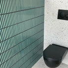 The Sevilla Mosaic Tiles, Original KitKat design in an Ocean Green, with a size of 20x145mm installed on the wall in a bathroom. A Black toilet is mounted to the adjacent wall.