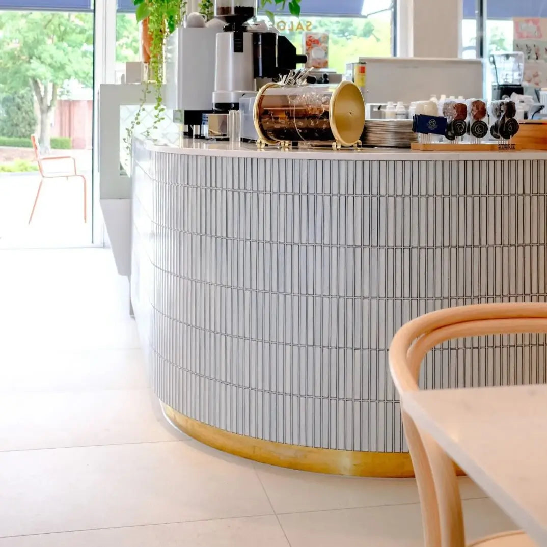 The Sevilla Mosaic Tiles, Original KitKat design in a white blue speckle, with a size of 20x145mm. Installed on a bar in a restaurant space. A coffee machine and various other hospitality equipment and utensils resting on top of the bar.