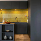 The Sevilla Mosaic Tiles, Original KitKat design in yellow, with a size of 20x145mm. Installed on the wall in the kitchen, surrounded by dark cabinetry.