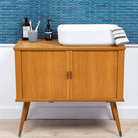 The Sevilla Mosaic Tiles, Oval design in Azure Blue, with a size of 23x98mm. Installed on a wall behind a console unit with a basin & hand towl, two tooth brushes in a cup, a hand soap and another product on the top